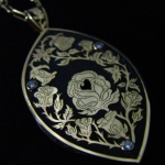 24 carat tanzanite set with blue and white diamonds in an 18k gold box-style pendant with a hand-fabricated chain. Designed by me... a one-of-a-kind piece with 100 hours of engraving work. The back has a mirror image of the same rose design with a heart-shape "viewer" of the very center ~ the heart~ of the tanzanite gem.