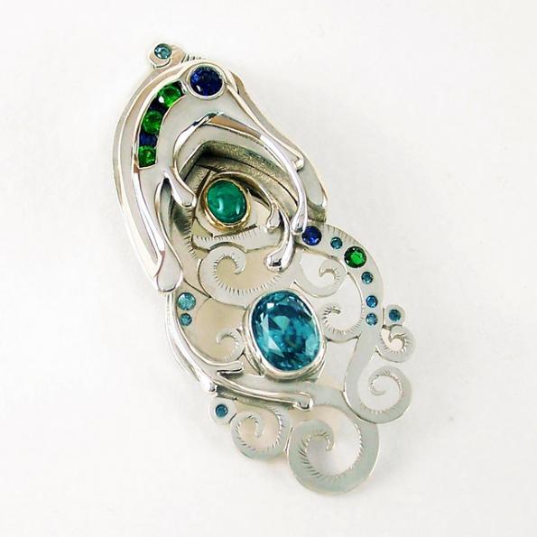 The piece includes a pierced and hand engraved Argentium base, a hollow form section on the top, hand pierced and sculpted drip accents, flush set gems, a channel setting section on the top, a tube set sapphire which also acts as the rivet which holds the top section together, a bezel set zircon and a 22k bezel set emerald cabochon.
Gems include cabbed emerald, blue diamonds, sapphire, chrome diopside and blue zircon. Mark created the channel setting on the top which holds a total of 5 gems.... 3 diopsides 2.4mm and 2 flush set sapphires 2mm. Entire piece was hand fabricated:)