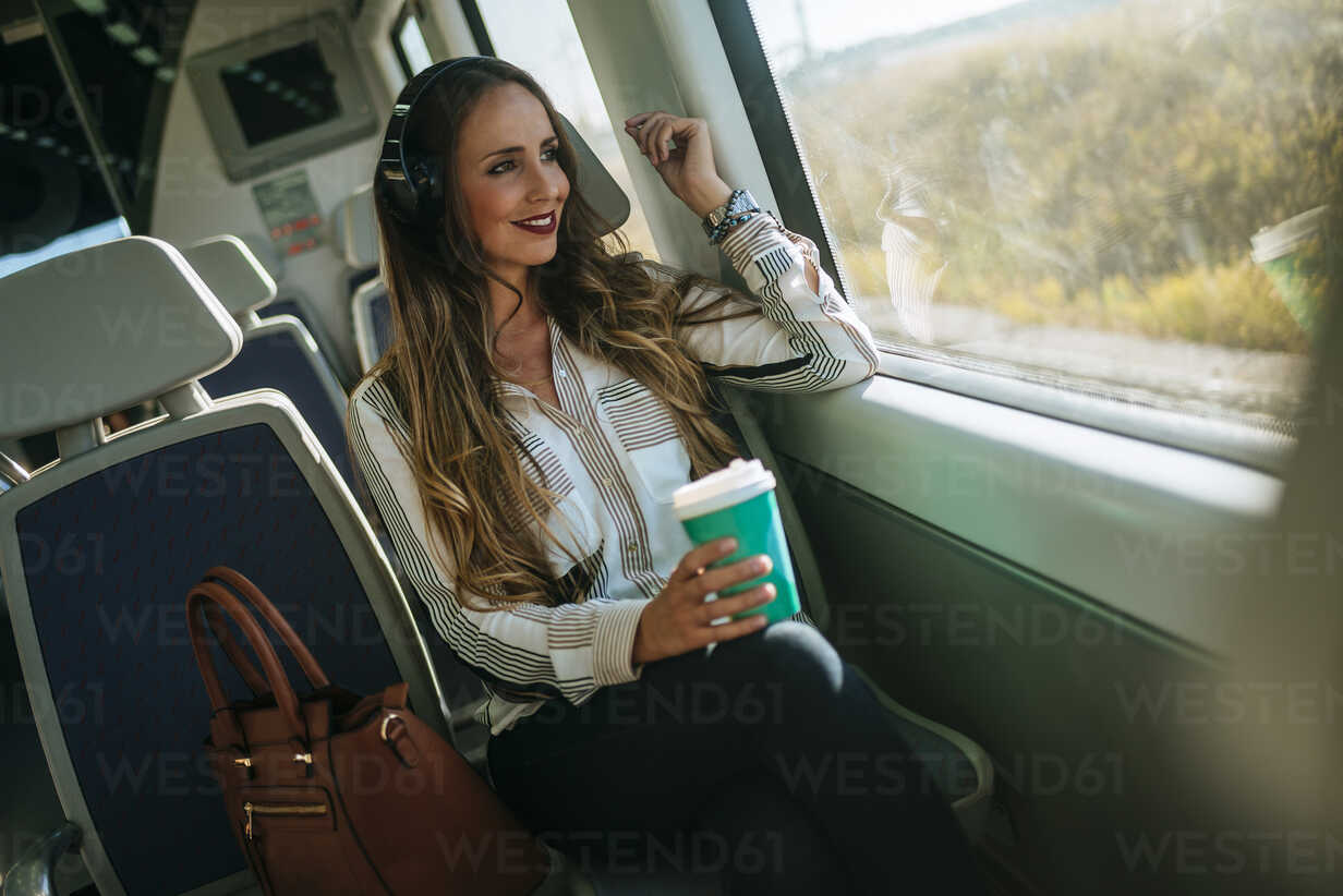 woman-on-a-train-listening-to-music-with-headphones-and-drinking-coffee-KIJF00873.jpg